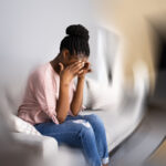 A woman sitting on a sofa, she is rubbing her temples, the room around her is blurry and spinning